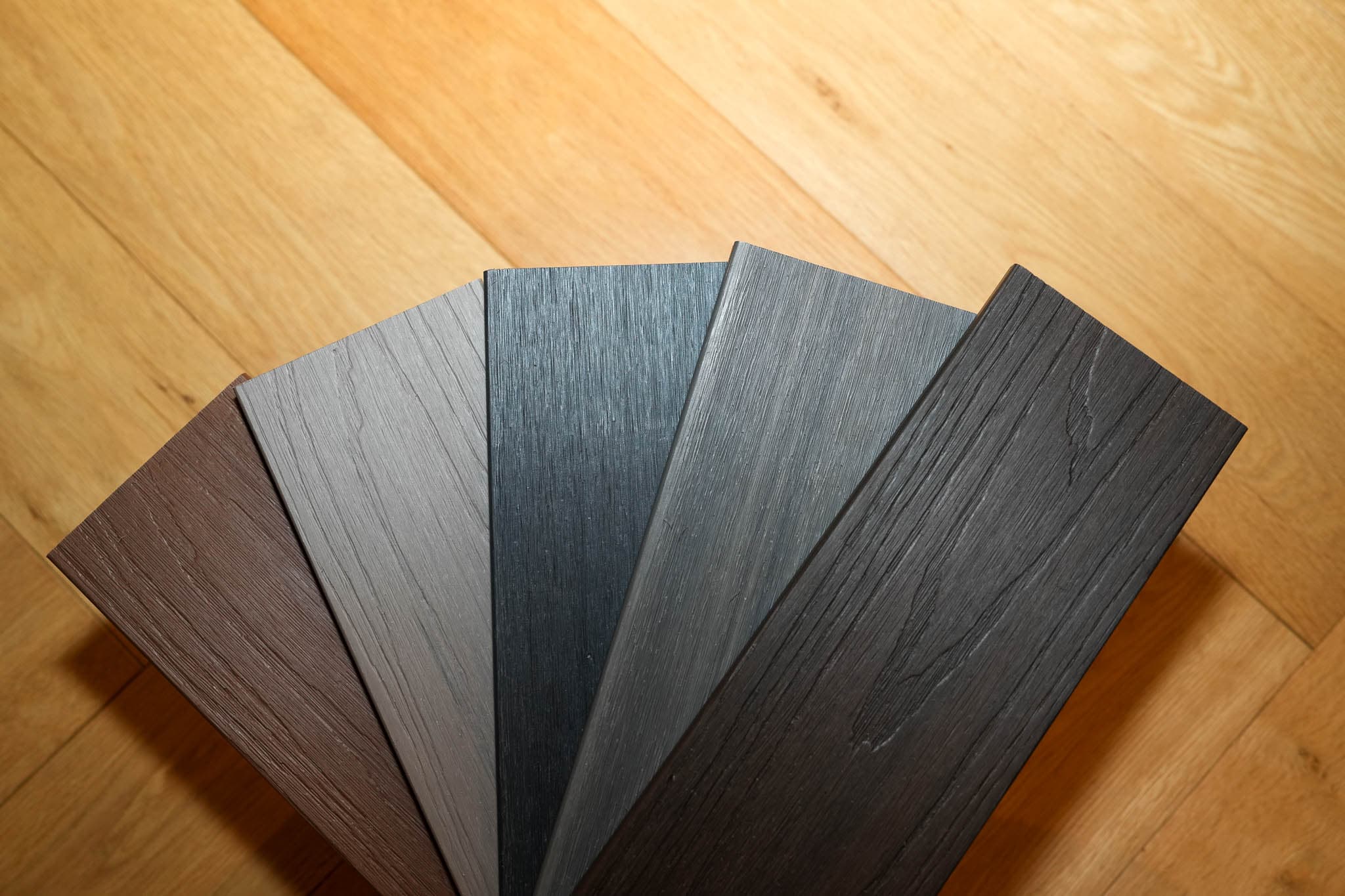 Fan of Hidecki decking sample colours on a wood floor